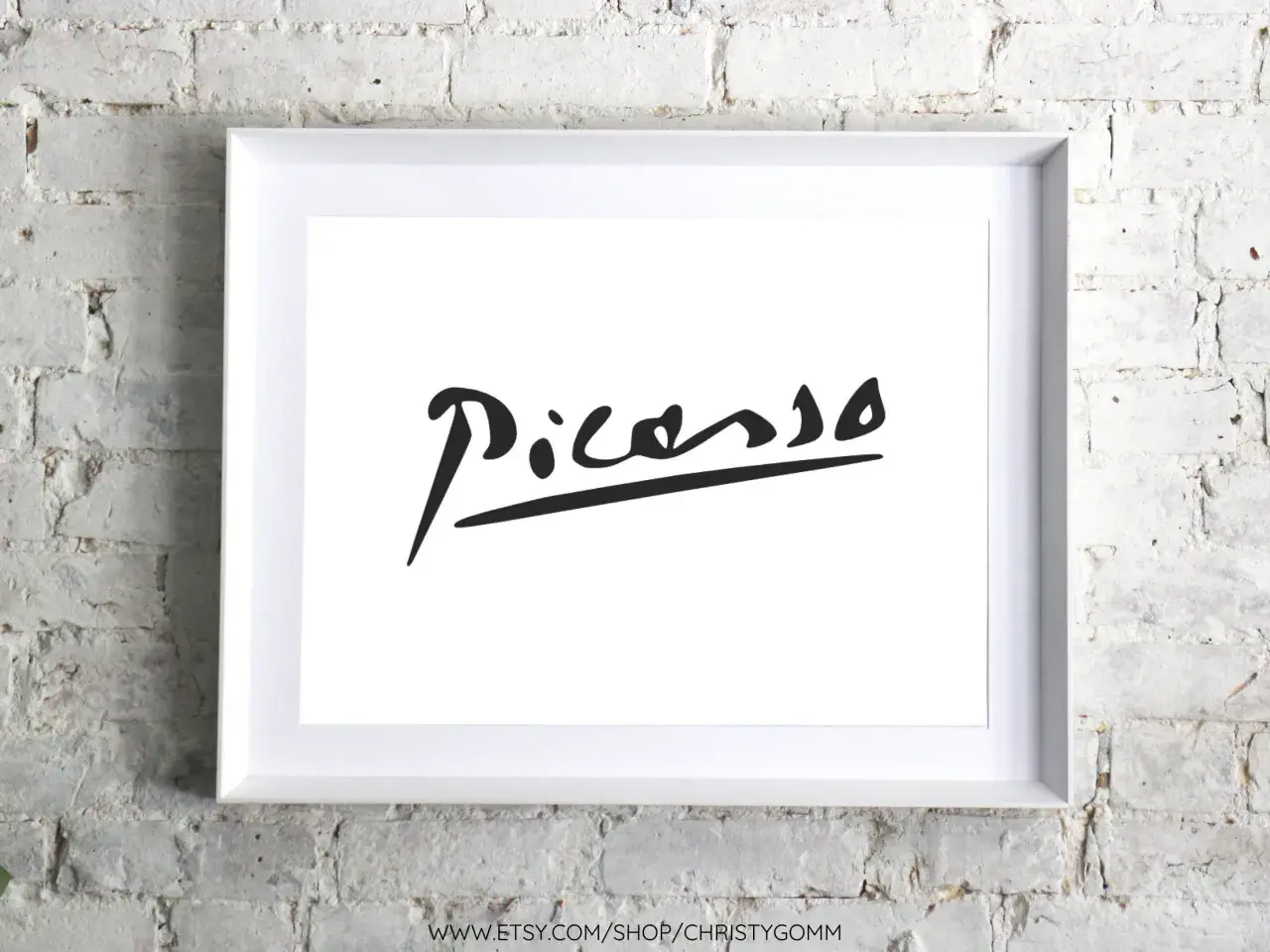 Firma pittore su tela, un'iconica firma di Picasso in nero su sfondo bianco, incorniciata in bianco, appesa a un muro di mattoni bianchi.