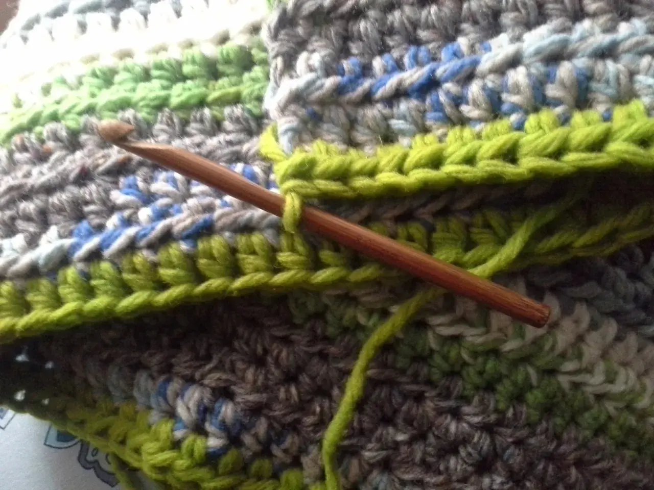 Coperta ai ferri con avanzi di lana, un'opera in corso con un uncinetto di legno che lavora maglie verdi su un tessuto multicolore.