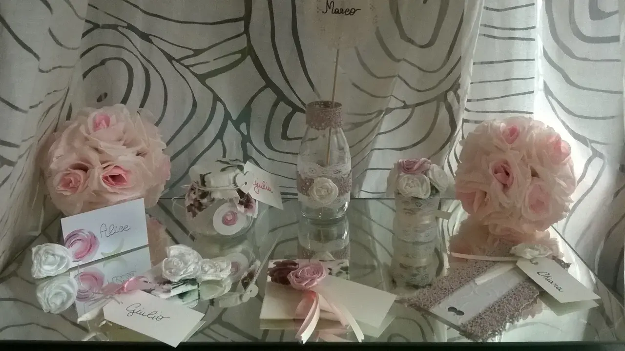 Segnaposto matrimonio fai da te shabby chic: rose rosa e bianche, vasetti decorati con pizzo, biglietti con nomi.