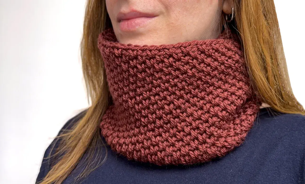 Donna con scaldacollo fai da te color mattone, lavorato a maglia, che le scalda il collo.