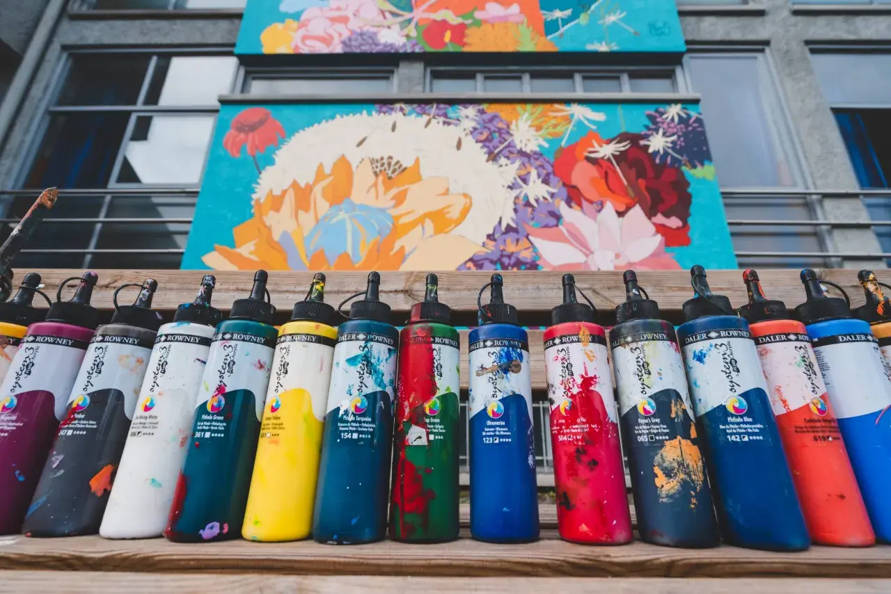 Flaconi di colori acrilici Daler Rowney, con vivaci **colori contrastanti** che riflettono la pittura floreale sullo sfondo.