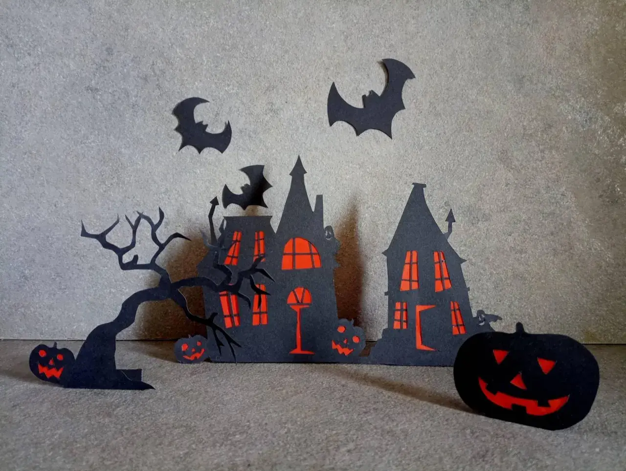 Scena di Halloween fai da te con case infestate, alberi spogli, pipistrelli e zucche intagliate.