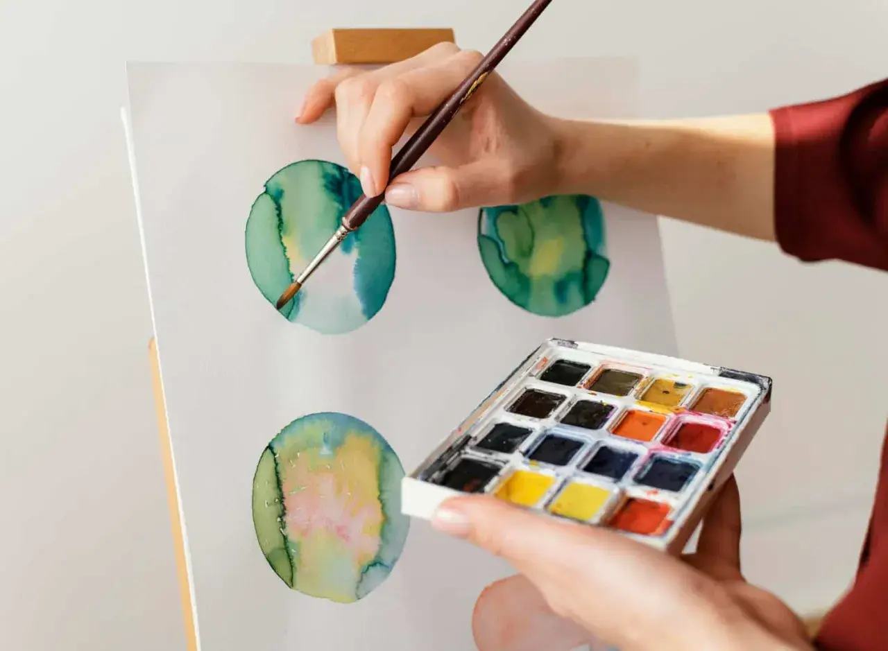 Mano che dipinge cerchi verdi e gialli con acquerello su tela. Palette di colori in primo piano.