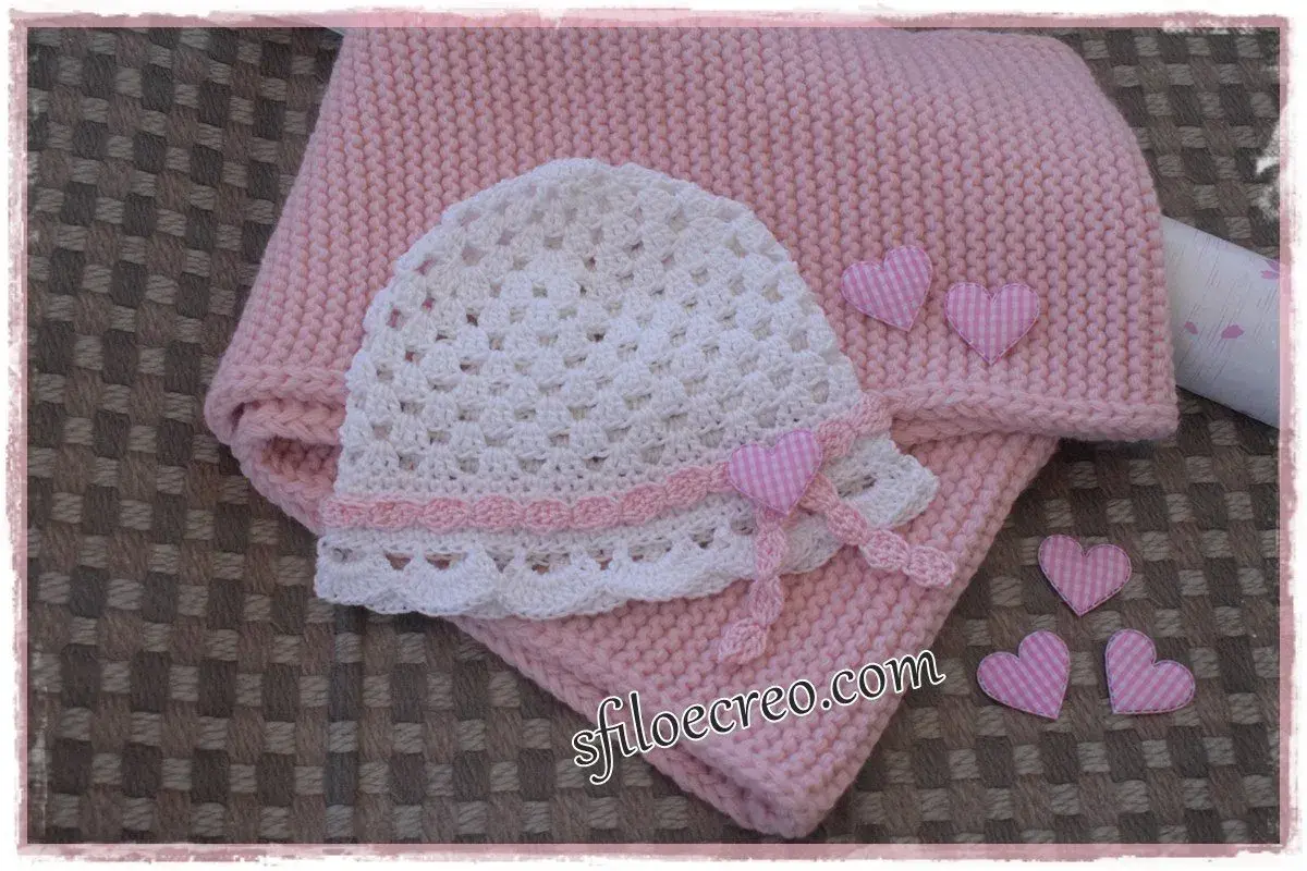 Schema maglia uncinetto bambina: cappellino bianco traforato e copertina rosa, decorati con cuoricini a quadretti.
