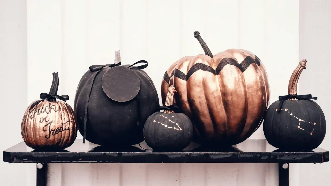 Cinque zucche decorate per Halloween: una colorata con "Trick or Treat", una grande color bronzo, e tre nere con disegni di costellazioni.
