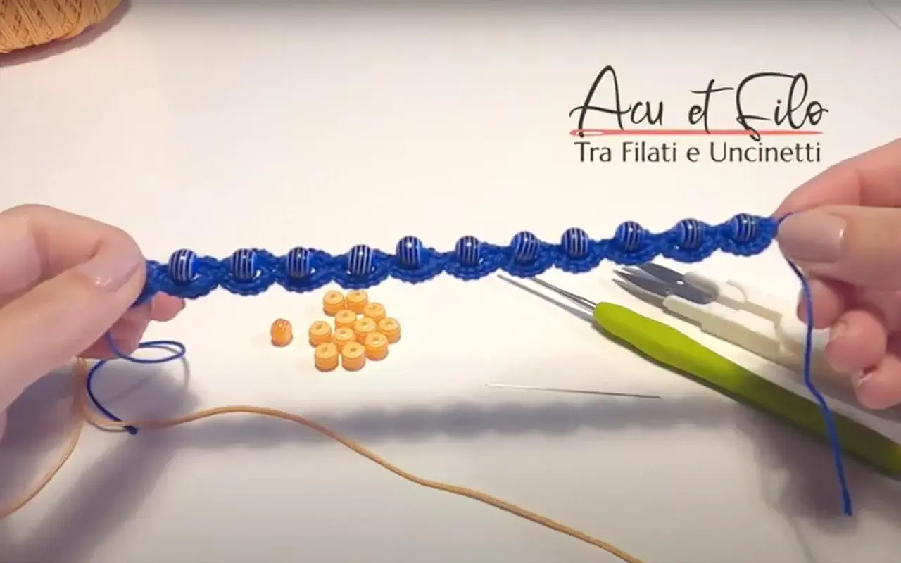 Bracciali all'uncinetto schemi gratis: un lavoro in corso con perline blu e arancioni, uncinetti e filo.