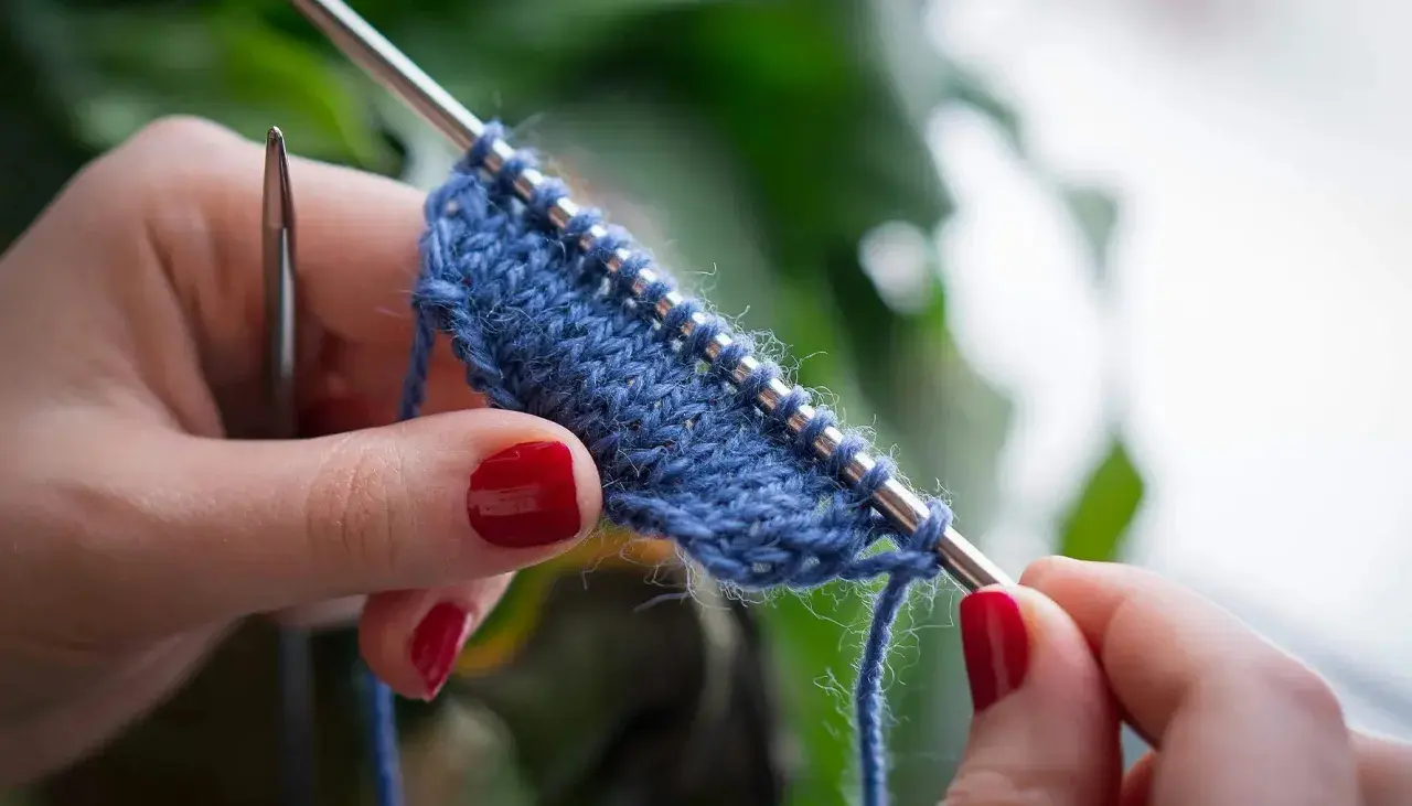 Mani con unghie rosse lavorano a maglia un filato blu. Impara come lavorare la lana con questo dettaglio ravvicinato.