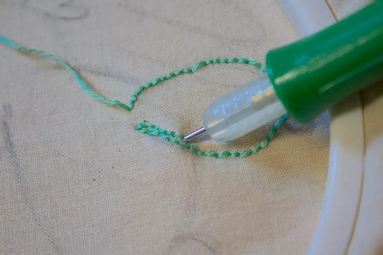 Ago magico crea schemi su stoffa, un punto alla volta, con filo verde brillante.