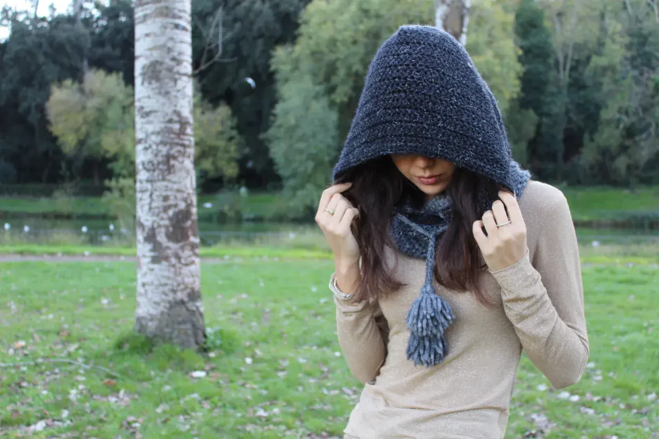 Donna con scaldacollo con cappuccio ai ferri, in un parco autunnale.