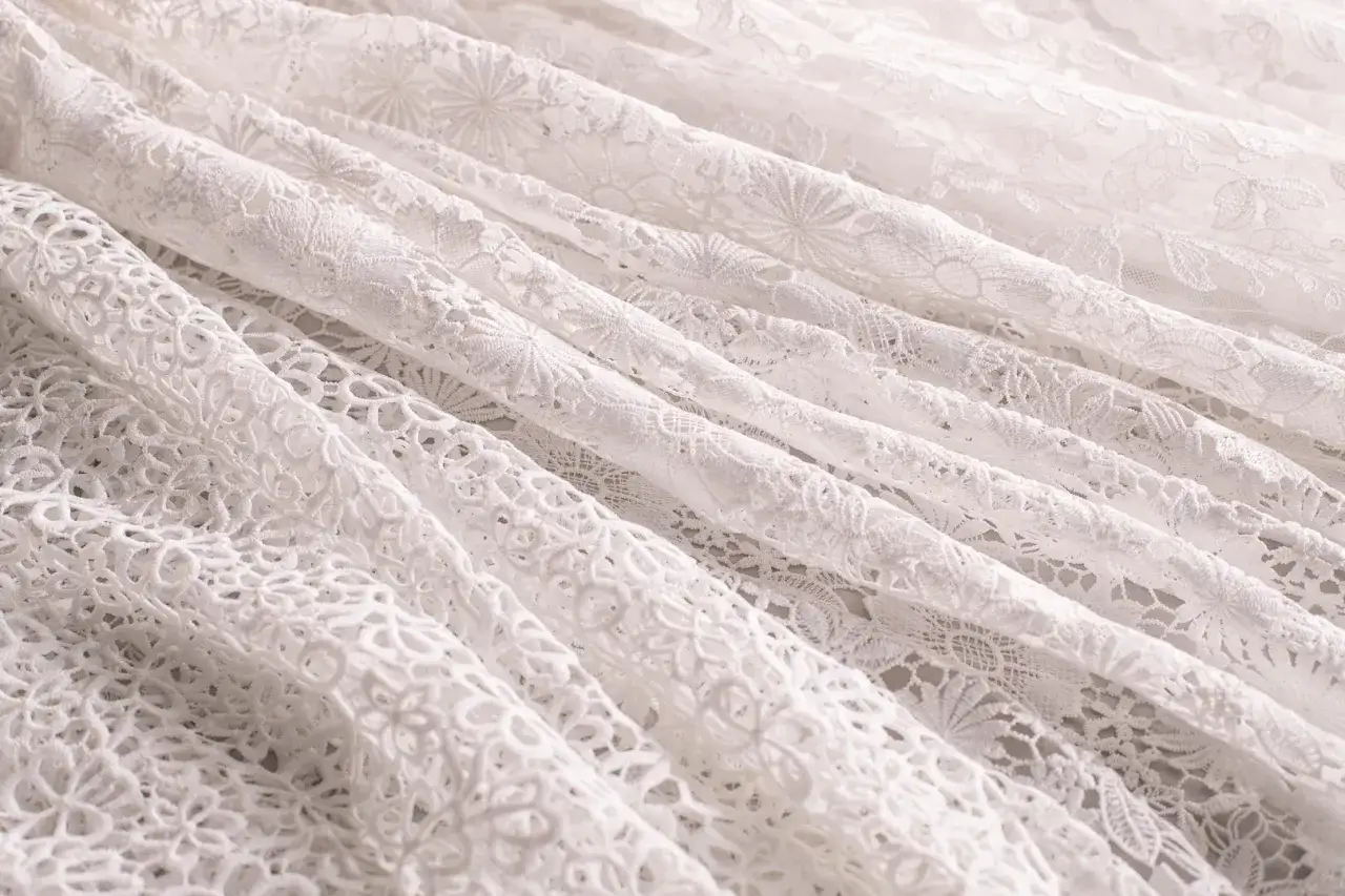 Tessuto in pizzo bianco, con pieghe morbide e motivi floreali intricati. Un materiale elegante e delicato.