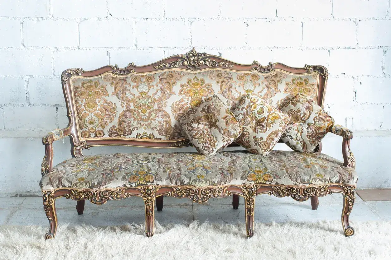Divano antico con un prezioso damascato tessuto, decorato con cuscini coordinati e finiture dorate.