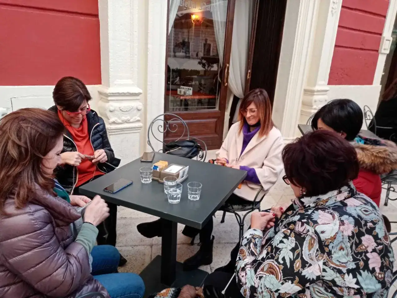Donne lavorano a maglia al cafe lana, chiacchierando sedute a un tavolino all'aperto.