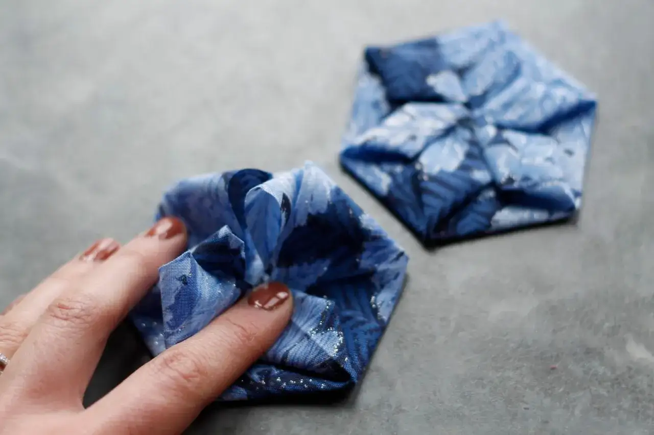 Mano che sistema una pieghetta di stoffa blu con fiori, un'altra simile sullo sfondo.