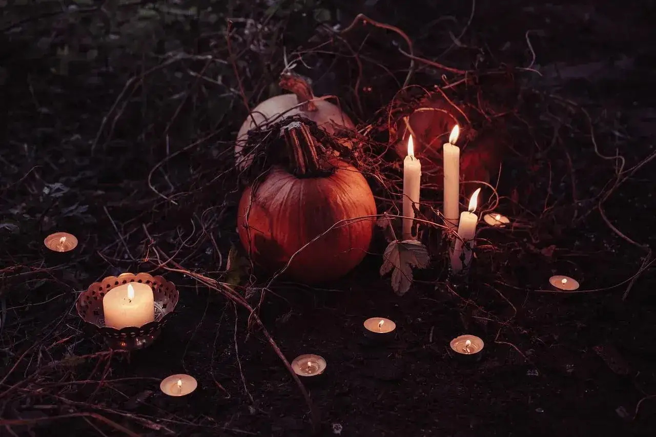 Un suggestivo centrotavola Halloween fai da te con zucche e candele accese tra rami secchi, crea un'atmosfera magica e spettrale.