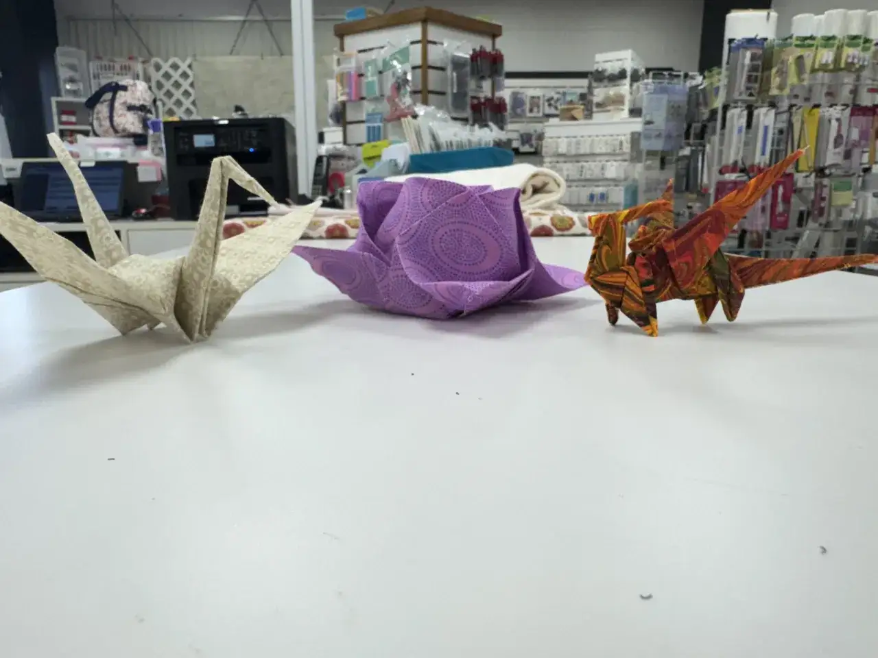 Gru, fiore e drago origami, ognuno con una pieghetta perfetta, su un tavolo bianco.