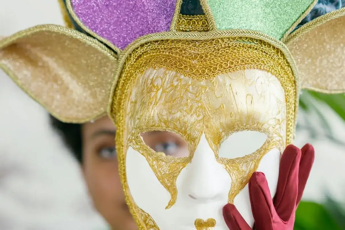 Maschera bianca e oro con decorazioni scintillanti, parte di elaborate decorazioni maschere carnevale. Una mano guantata la tiene.