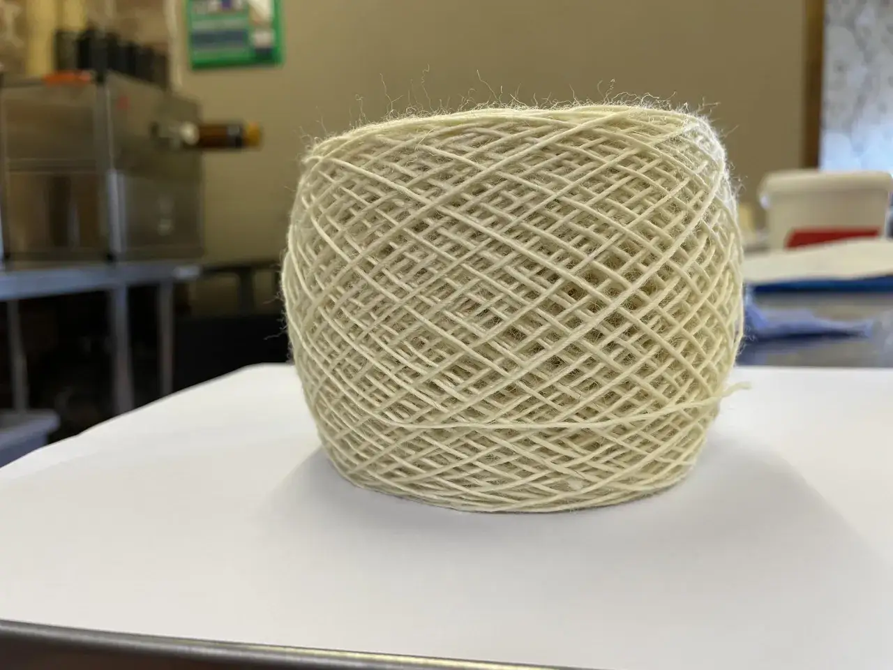 Un gomitolo di lana d'agnello color crema, con fili sottili che spuntano, pronto per essere trasformato in qualcosa di caldo e accogliente.