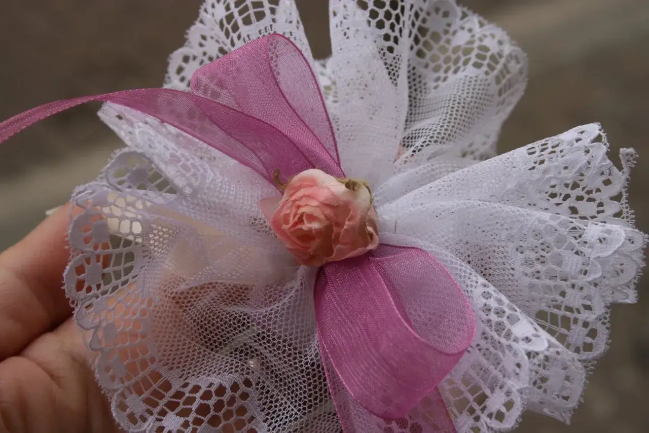 Fiocchi per bomboniere in pizzo bianco con nastro rosa e un piccolo bocciolo di rosa.