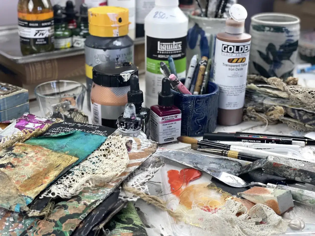 Tavolo da lavoro con barattoli di medium acrilico, pennelli, colori e collage.