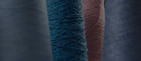 Gomitoli di filato color petrolio e rosa, pronti per creare maglioni pregiati.