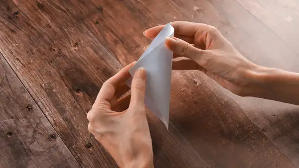 Mani che creano una pieghetta su un foglio di carta bianca, su un tavolo di legno scuro.