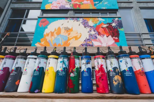 Flaconi di colori acrilici Daler Rowney, con vivaci **colori contrastanti** che riflettono la pittura floreale sullo sfondo.