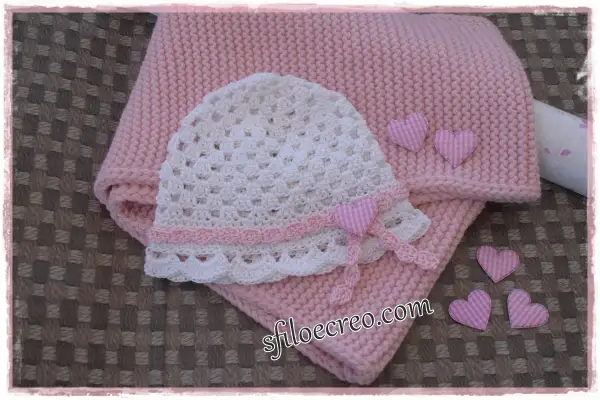 Schema maglia uncinetto bambina: cappellino bianco traforato e copertina rosa, decorati con cuoricini a quadretti.