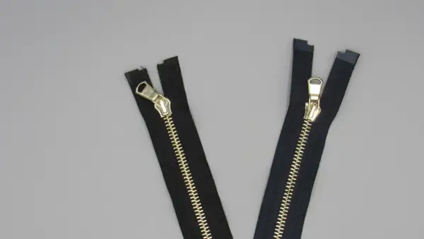 Due cerniere lampo eleganti nere con dettagli dorati su sfondo grigio.