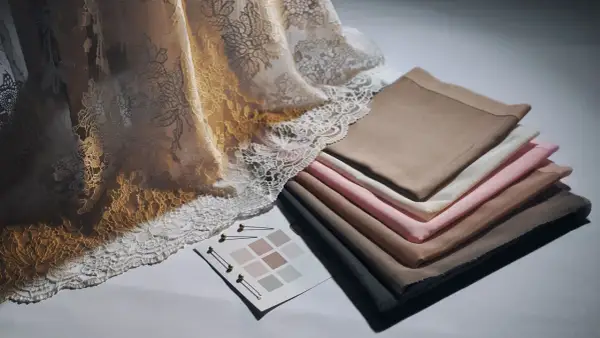 Tessuti pregiati: un drappo di pizzo dorato e avorio accanto a campioni di tessuti color carne, rosa e grigio.
