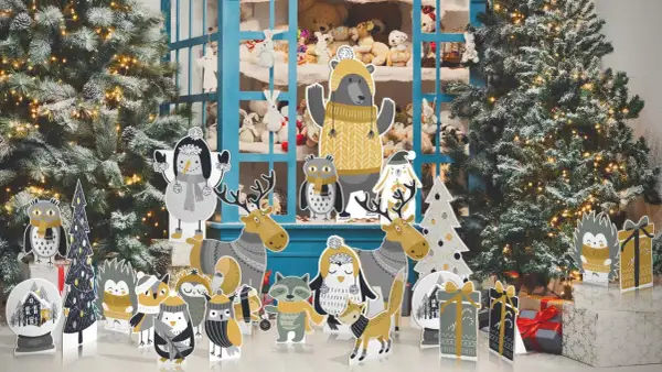 Sagome natalizie grandi di animali e alberi, con un orso al centro, davanti a un albero di Natale innevato e una vetrina piena di peluche.
